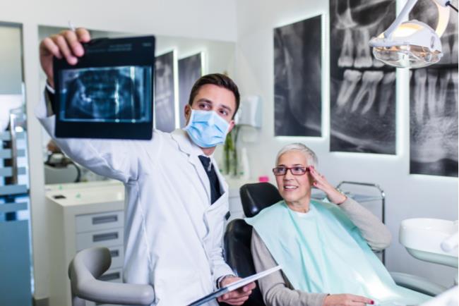 רופא שיניים מסביר לאישה על צילומי השיניים במהלך בדיקת רופא שיניים תקופתית